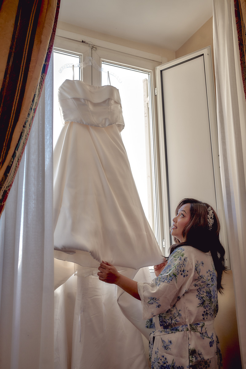 Bride holding wedding dress by the window
