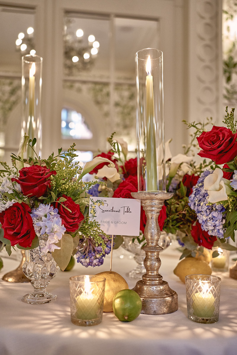 Detail of wedding table at Hotel De La Ville with green candles and red and light blue flowers