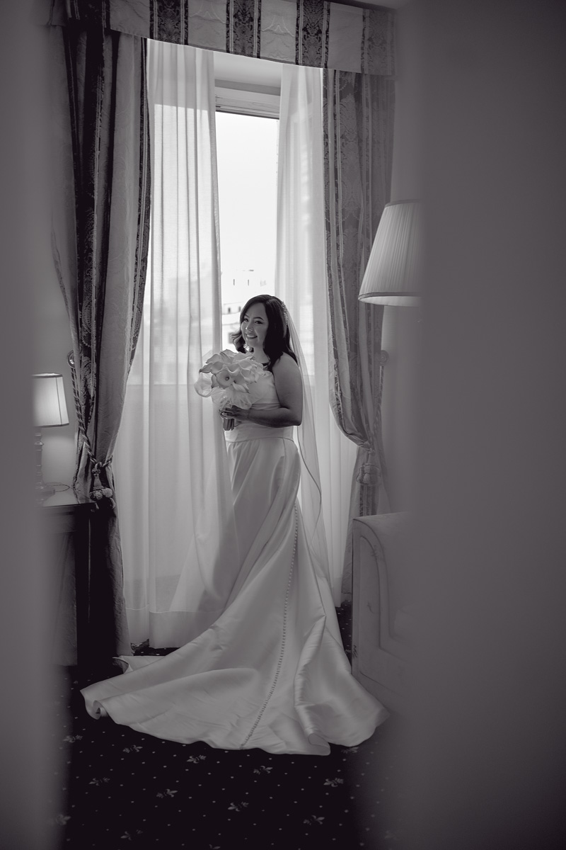 Black and white picture of bride in wedding dress by the window